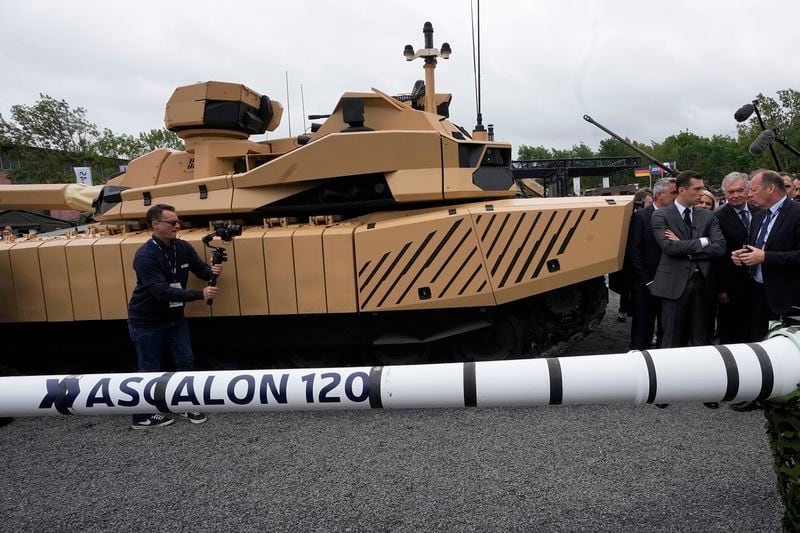 Jordan Bardella, second right, president of the far-right National Front party, listens to explanations next to a Leclerc Evolution battle tank and a Ascalon 120mm gun at the Eurosatory Defense and Security exhibition, Wednesday, June 19, 2024 in Villepinte, north of Paris. Jordan Bardella, hoping to become France's prime minister, appealed Tuesday to voters to hand his party a clear majority after French President Emmanuel Macron's announcement on June 9 that he was dissolving France's National Assembly, parliament's lower house.( AP Photo/Michel Euler)