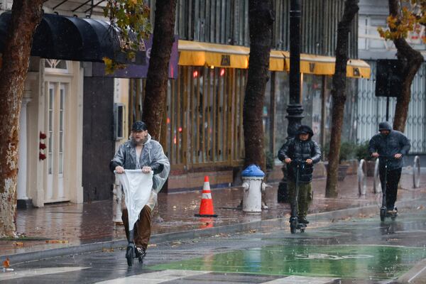 A scooter rider wears a poncho and a plastic bag as a rain cover for the handlebars as they and other scooter riders battle the rain as they ride along Market Street, Friday, Nov. 22, 2024 in San Francisco, Calif. (Lea Suzuki/San Francisco Chronicle via AP)