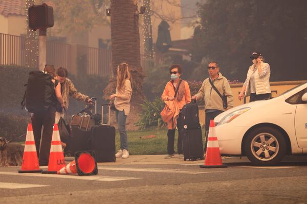 People wait with some belongings while fleeing the Palisades Fire in the Pacific Palisades neighborhood of Los Angeles, Tuesday, Jan. 7, 2025. (AP Photo/Etienne Laurent)