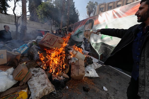 A banner with an image depicting the ousted Syrian President Bashar Assad is placed on the fire as a Syrian member of the rebel forces destroys drugs and alcoholic beverages, found at a complex building, in Damascus, Syria, Wednesday, Dec. 25, 2024. (AP Photo/Omar Sanadiki)