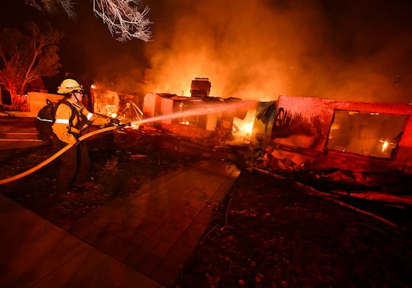 A firefighter from Costa Mesa works to extinguish a fire burning a home on Valleylights Drive during the Eaton fire in the Hastings Ranch community of Pasadena, Calif., early Wednesday, Jan. 8, 2025. (Will Lester/The Orange County Register via AP)