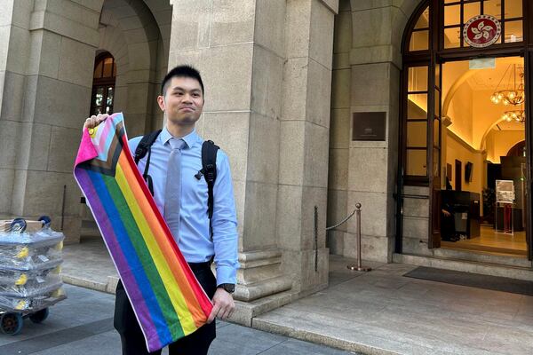 Nick Infinger, who won a years-long legal battle over the differential treatment facing same-sex couples, holds up a rainbow banner after speaking to media members outside Hong Kong’s top court on Tuesday, Nov. 26, 2024. (AP Photo/Kanis Leung)