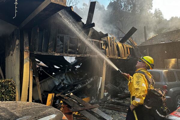 A firefighter hoses down hot spots around a fire-ravaged property after the Franklin Fire swept through Tuesday, Dec. 10, 2024, in Malibu, Calif. (AP Photo/Eugene Garcia)