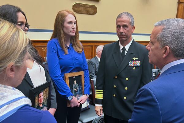 FILE - Amber Sax, center, holds a photo of her late husband, Marine Corps MV-22B pilot Capt. John Sax, as she and other family members who have lost service members to Osprey crashes talk with Vice Adm. Carl Chebi, Commander of U.S. Naval Air Systems Command, center right, and Peter Belk, acting Assistant Secretary of Defense for Readiness, right, before a hearing on the programs safety record, Wednesday, June 12, 2024, on Capitol Hill in Washington. (AP Photo/Tara Copp)