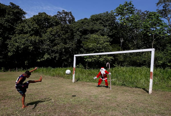 A young Amazonian resident strikes a ball towards Jorge Barroso, dressed as Santa Claus, who gave the ball to the boy after Barroso arrived on a boat to distribute Christmas gifts to children, in Iranduba, Brazil, Saturday, Dec. 21, 2024. (AP Photo/Edmar Barros)