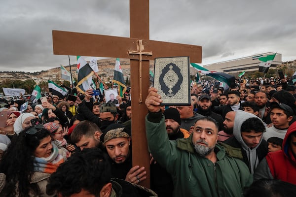 Syrians hold a copy of the Quran next to a Christian cross during a demonstration in support of unity among minorities and the ousting of the Bashar Assad government in Umayyad Square, in Damascus, Syria, Friday, Dec. 27, 2024. (AP Photo/Omar Sanadiki)