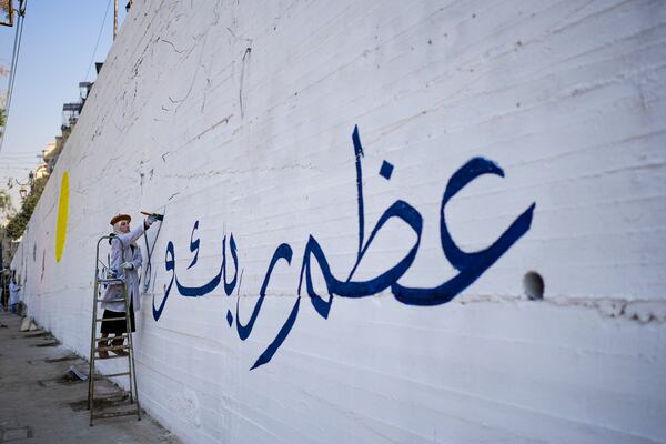 A girl writes "Worship your God" in Arabic as a group of young volunteers paints a mural symbolizing peace on a wall on the outskirts of Damascus, Syria, Sunday Jan. 12, 2025. (AP Photo/Mosa'ab Elshamy)