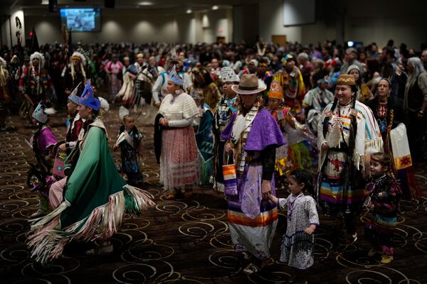 Tiffany Stuart, at right in white, holds hands with her daughter Kwestaani Chuski Stuart, bottom right, as they participate in a powwow at Chinook Winds Casino Resort, Saturday, Nov. 16, 2024, in Lincoln City, Ore. (AP Photo/Jenny Kane)