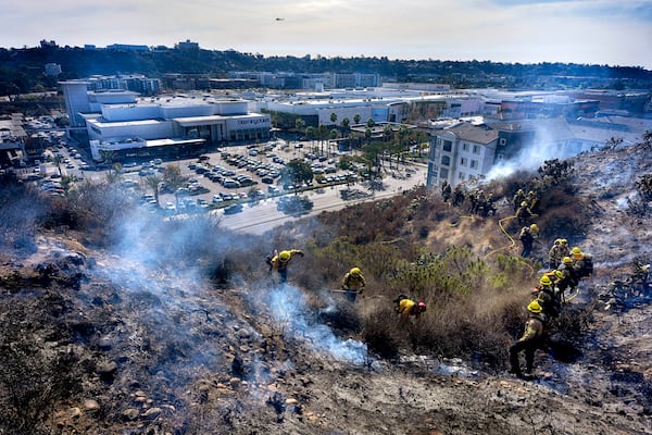 San Diego firefighters knock down a small brush along a hillside over the Mission Valley Shopping Mall in San Diego on Tuesday, Jan. 21, 2025. (AP Photo/Gregory Bull)