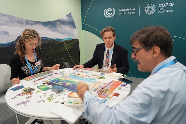 Courtney Howard, of Global Climate and Health Alliance and Nathan Cogswell, of World Resources Institute, center, play Daybreak, a game where players are supposed to work together to find a way to curb climate change, with Seth Borenstein, Associated Press science writer, at the COP29 U.N. Climate Summit, Tuesday, Nov. 19, 2024, in Baku, Azerbaijan. (AP Photo/Joshua A. Bickel)