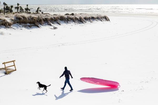 A man and his dog enjoy the beach after a winter storm dropped ice and snow Wednesday, Jan. 22, 2025, on the Isle of Palms, S.C. (AP Photo/Mic Smith)