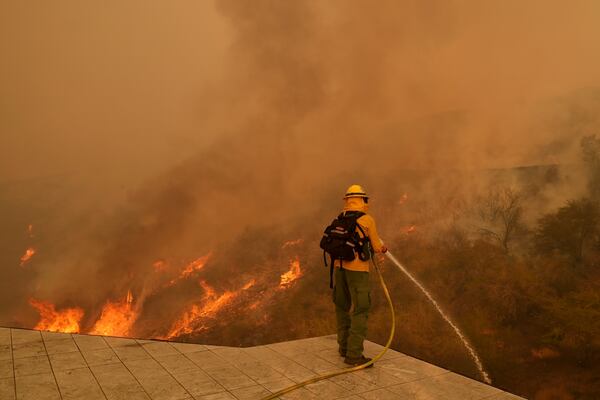 FILE - A firefighter hoses down flames as the Palisades Fire approaches in Mandeville Canyon, Jan. 11, 2025, in Los Angeles. (AP Photo/Jae C. Hong,File)