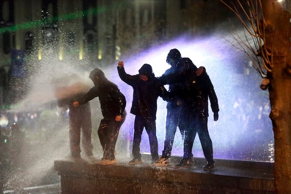 Demonstrators stand atop of a tomb under running water from a water cannon during a protests against the government's decision to suspend negotiations on joining the European Union, outside the parliament's building in Tbilisi, Georgia, on Monday, Dec. 2, 2024. (AP Photo/Zurab Tsertsvadze)