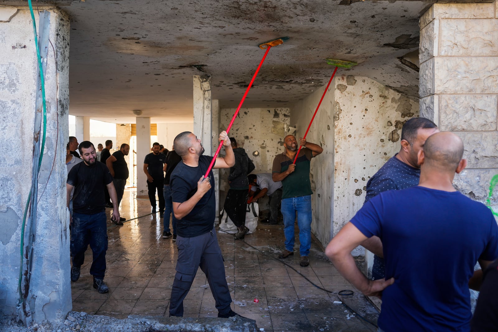 Neighbors clean blood stains from the ceiling of a damaged house where one person was killed after a projectile launched from Lebanon slammed into Maalot-Tarshiha, northern Israel, Tuesday, Oct. 29, 2024. (AP Photo/Ohad Zwigenberg)