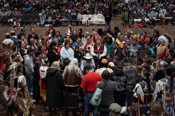 People gather around Chet Clark, in the white hat at center, as he plays an honor song for the Confederated Tribes of Siletz Indians during a powwow at Chinook Winds Casino Resort, Saturday, Nov. 16, 2024, in Lincoln City, Ore. Chet, of the drum group Johonaaii, wrote the song in 2007 and sang it for the first time during the tribe's 30th restoration powwow. It has been sung during every restoration powwow since then. (AP Photo/Jenny Kane)