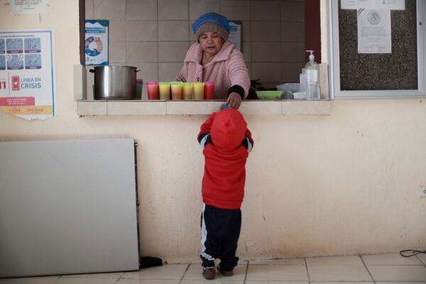 Roxana, a migrant from Chiapas, Mexico, who preferred to omit her last name, hands a child a drink at El Buen Samaritano shelter, in Ciudad Juarez, Mexico, Monday, Jan. 20, 2025, the inauguration day of President Donald Trump. (AP Photo/Christian Chavez)