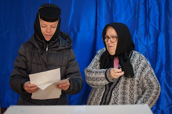 An elderly woman with poor eye sight holds a stamp after getting help from her daughter, an Orthodox nun, left, to cast her vote in the country's presidential elections, in Pasarea, Romania, Sunday, Nov. 24, 2024. (AP Photo/Vadim Ghirda)