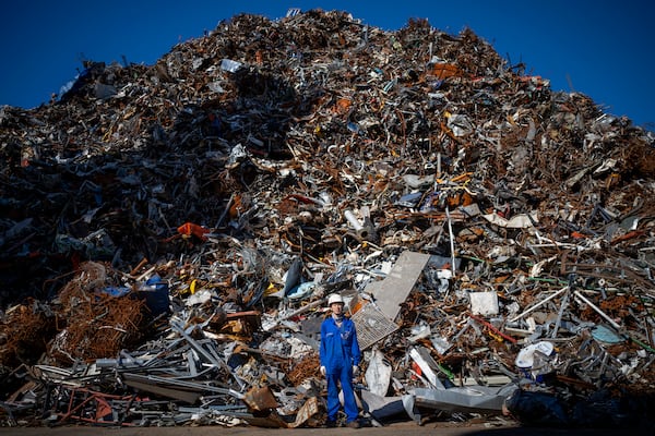 Ma Aijun, 45, of China, poses next to a mountain of scrap metal unloaded from the Chinese merchant ship he works on, at the port of Barcelona, Spain, Friday, Sept. 27, 2024. (AP Photo/Emilio Morenatti)