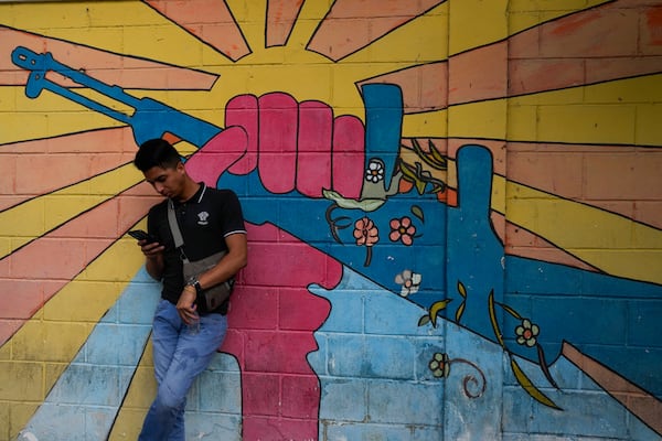 A government supporter rests in front of a mural before the ceremony to open the legislative year in Caracas, Venezuela, Sunday, Jan. 5, 2025. (AP Photo/Matias Delacroix)