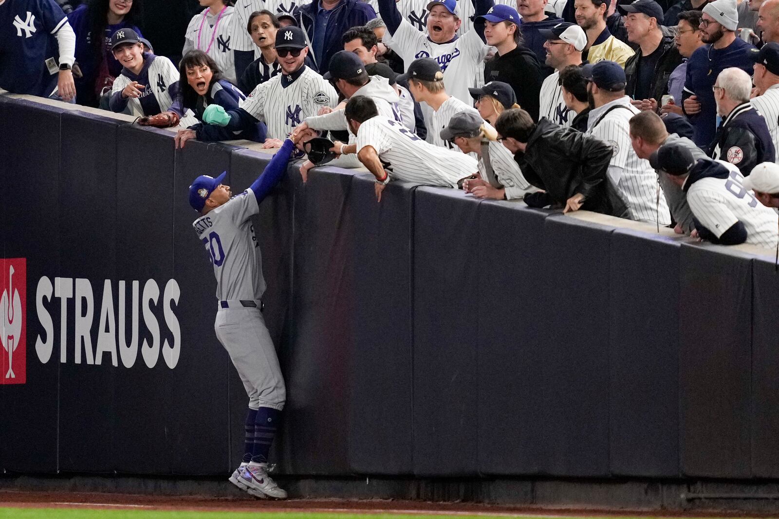 Fans interfere with a foul ball caught by Los Angeles Dodgers right fielder Mookie Betts during the first inning in Game 4 of the baseball World Series against the New York Yankees, Tuesday, Oct. 29, 2024, in New York. (AP Photo/Ashley Landis)