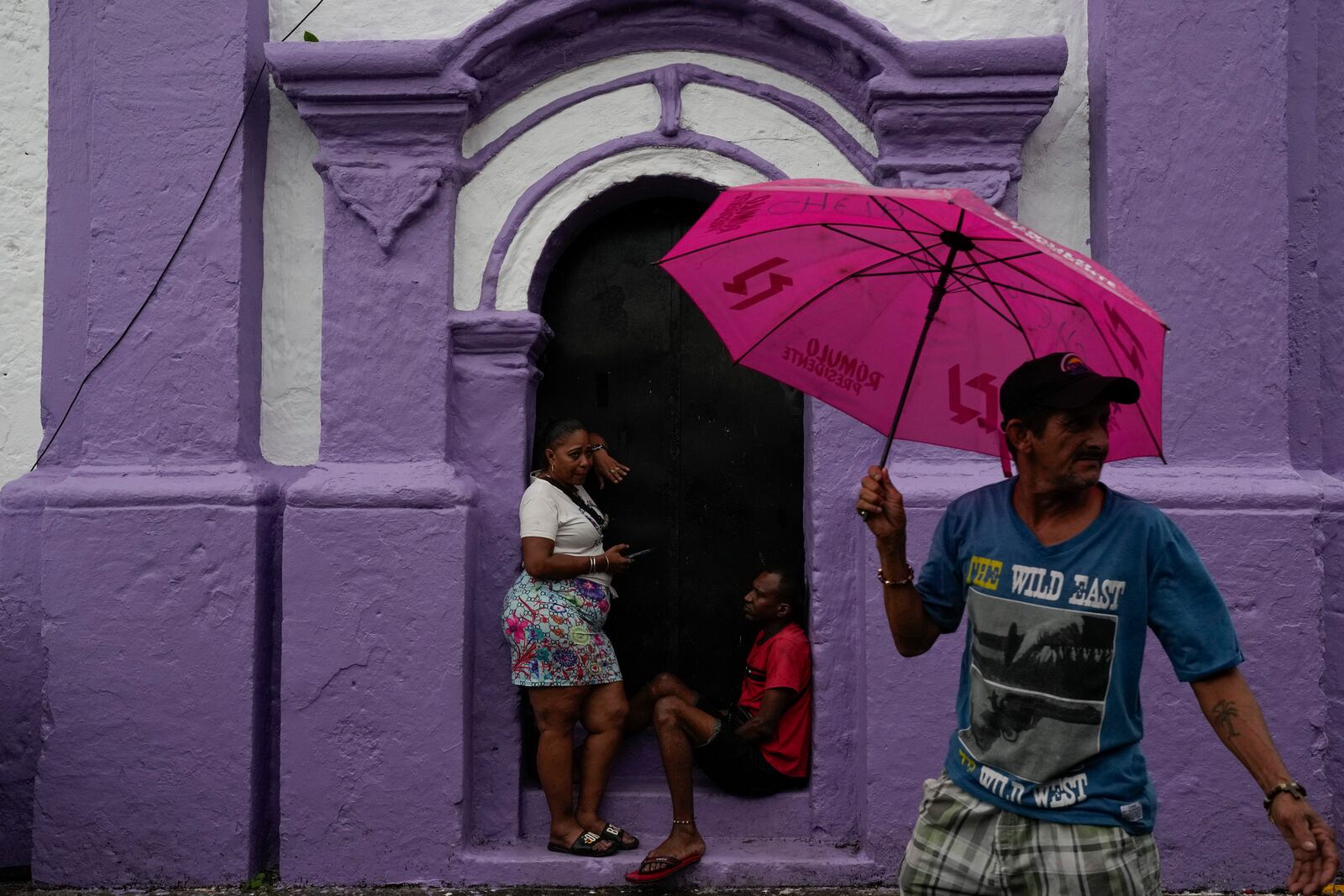 People take cover from rain at San Felipe Church in Portobelo, Panama, Sunday, Oct. 20, 2024, a day before the Black Christ festival. (AP Photo/Matias Delacroix)