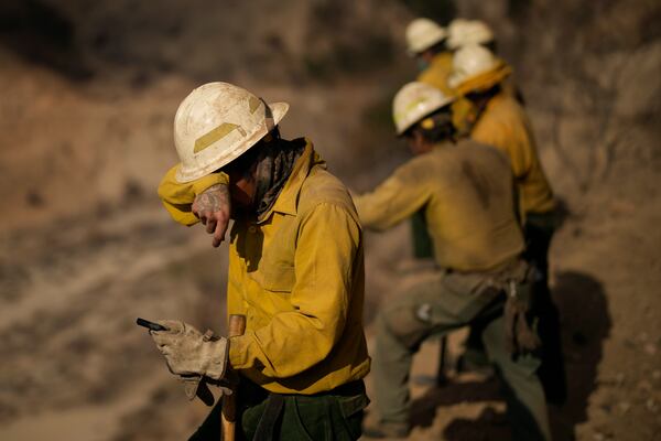 Anthony Platero, a member of the Navajo Scouts firefighter crew, wipes dust from his eyes as he clears debris from a landslide across a road on a hillside at the Eaton Fire, Friday, Jan. 17, 2025, in Altadena, Calif. (AP Photo/John Locher)