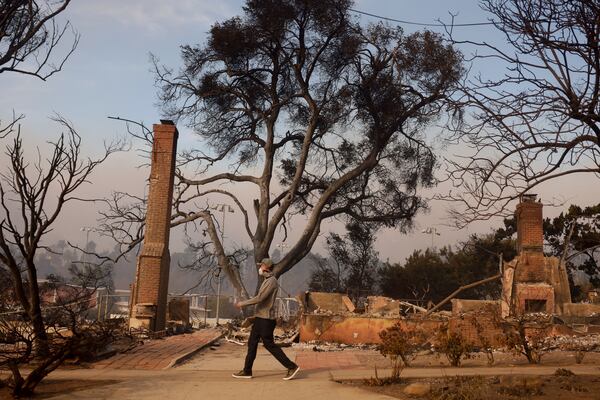 A person walks past a fire-ravaged property after the Palisades Fire swept through in the Pacific Palisades neighborhood of Los Angeles, Wednesday, Jan. 8, 2025. (AP Photo/Etienne Laurent)