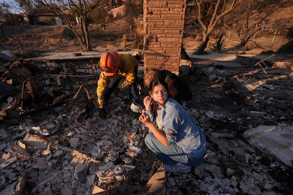 Ella Venne, front, holds a cup she found in the remains of her family's home destroyed by the Eaton Fire as she searches with Glendale Fire Department captain Chris Jernegan, left, and his wife Alison in Altadena, Calif., Saturday, Jan. 11, 2025. (AP Photo/Mark J. Terrill)