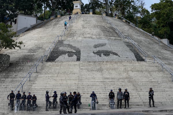 Bolivarian National Police stand guard in front of steps featuring a giant portrait of the eyes of the late President Hugo Chavez ahead of President Nicolas Maduro's swearing-in for a third term, in Caracas, Venezuela, Sunday, Jan. 5, 2025. (AP Photo/Matias Delacroix)