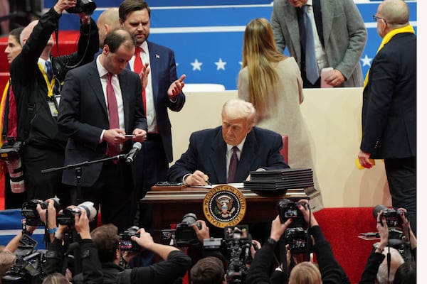 President Donald Trump signs an executive order as Vice President JD Vance watches at an indoor Presidential Inauguration parade event in Washington, Monday, Jan. 20, 2025. (AP Photo/Matt Rourke)