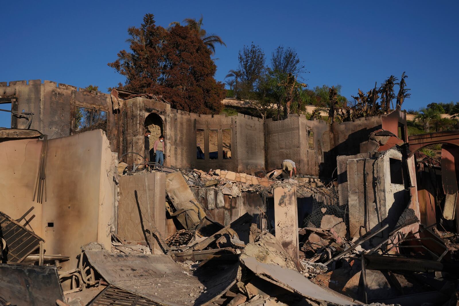 Heidi Nardoni, at right in doorway, and family friends search her home destroyed by the Mountain Fire in Camarillo, Calif., Friday, Nov. 8, 2024. (AP Photo/Jae C. Hong)