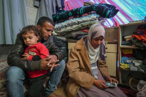 Areej al Qadi, right, shows a picture of one of her three dead children as her husband Mahmoud bin Hassan, left, holds a fourth surviving child at their tent in a refugee camp in Deir al-Balah, Gaza Strip, Thursday Nov. 21, 2024. Seven-year-old Hamza, his five-year-old brother Abdelaziz, and his four-year-old sister Laila Hassan were among 9 people killed by an Israeli strike in Khan Younis on Wednesday. Palestinian health officials say the death toll in the Gaza Strip from the 13-month-old war between Israel and Hamas has surpassed 44,000. (AP Photo/Abdel Kareem Hana)