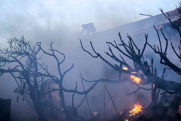 A firefighter tries to contain the Palisades Fire from a rooftop in the Pacific Palisades neighborhood of Los Angeles, Tuesday, Jan. 7, 2025. (AP Photo/Ethan Swope)