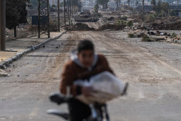 A boy carrying bread cycles home as Israeli military armored vehicles block a road leading to the town of Quneitra, Syria, Sunday, Jan. 5, 2025. (AP Photo/Mosa'ab Elshamy)