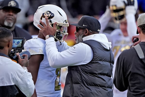 Colorado head coach Deion Sanders talks to quarterback Shedeur Sanders (2) before an NCAA college football game against Kansas, Saturday, Nov. 23, 2024, in Kansas City, Mo. (AP Photo/Charlie Riedel)