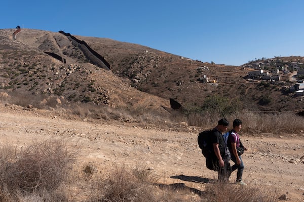 Two men walk down a road towards Border Patrol agents after crossing the border illegally through a gap in two walls separating Mexico from the United States, behind, before turning themselves in, Thursday, Jan. 23, 2025, in San Diego. (AP Photo/Gregory Bull)