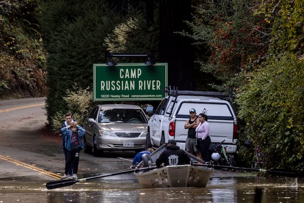 Residents watch as Ben Cote rows a boat across a flooded Neely road after a major storm in Guerneville, Calif., Saturday, Nov. 23, 2024. (Stephen Lam/San Francisco Chronicle via AP)