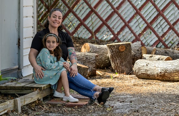 Cecila Grove and her daughter Aria Grove sit outside their home Saturday, Nov. 16, 2024, in Sarasota, Fla., next to limbs from a tree that fell durring the recent hurricanes. (AP Photo/Steve Nesius)