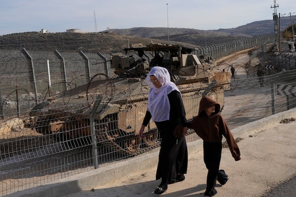 A woman and child walk past Israeli armored vehicles parked near the "Alpha Line" that separates the Israeli-annexed Golan Heights from Syria, in the town of Majdal Shams, Monday, Dec. 9, 2024. (AP Photo/Matias Delacroix)