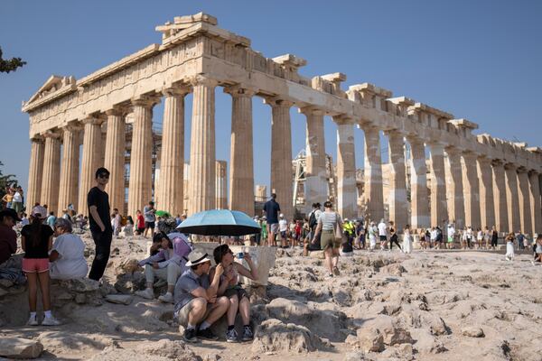 FILE - A tourist drinks water as she and a man sit under an umbrella in front of the five century BC Parthenon temple at the Acropolis hill during a heat wave, on July 13, 2023. (AP Photo/Petros Giannakouris, File)