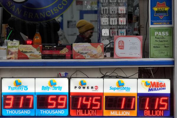 Rina Flores, middle, works behind the counter over a sign advertising the estimated $1.15 billion Mega Millions jackpot, bottom right, at Rossi's Deli in San Francisco, Thursday, Dec. 26, 2024. (AP Photo/Jeff Chiu)