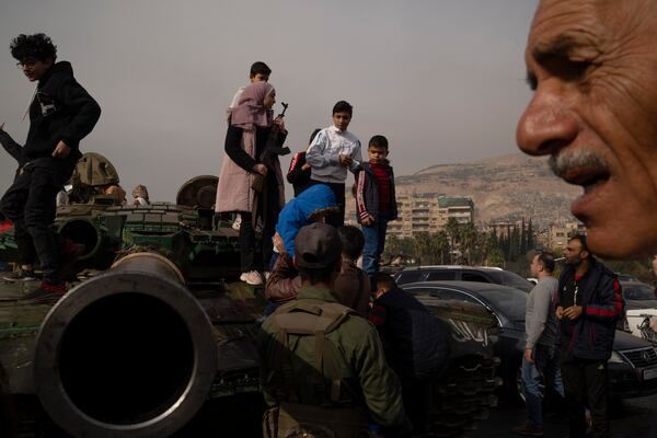 A youth, holding a rifle borrowed from a Syrian opposition fighter people, poses for a picture on the top of a government forces tank that was left on a street, at the Umayyad Square in Damascus, Syria, Wednesday, Dec. 11, 2024. (AP Photo/Leo Correa)