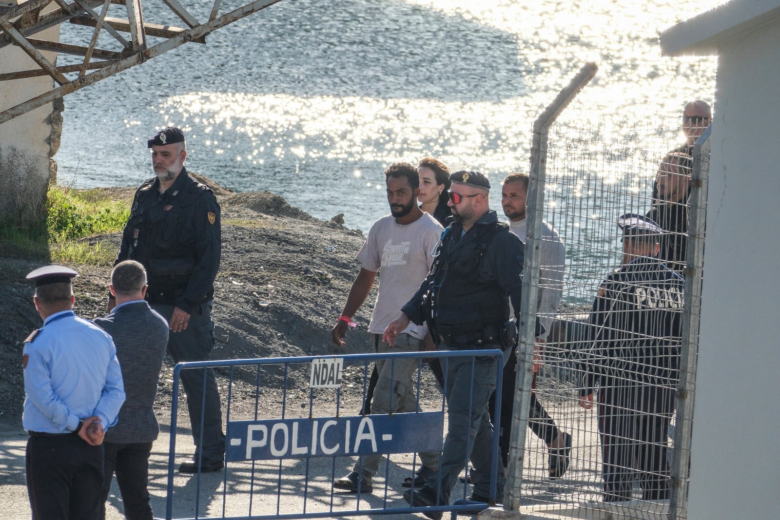 Migrants and security officials walk at the port of Shengjin, northwestern Albania. Wednesday, Oct. 16, 2024 after disembarking from the Italian navy ship Libra, carrying the first group of 16 migrants intercepted in international waters. (AP Photo/Vlasov Sulaj)