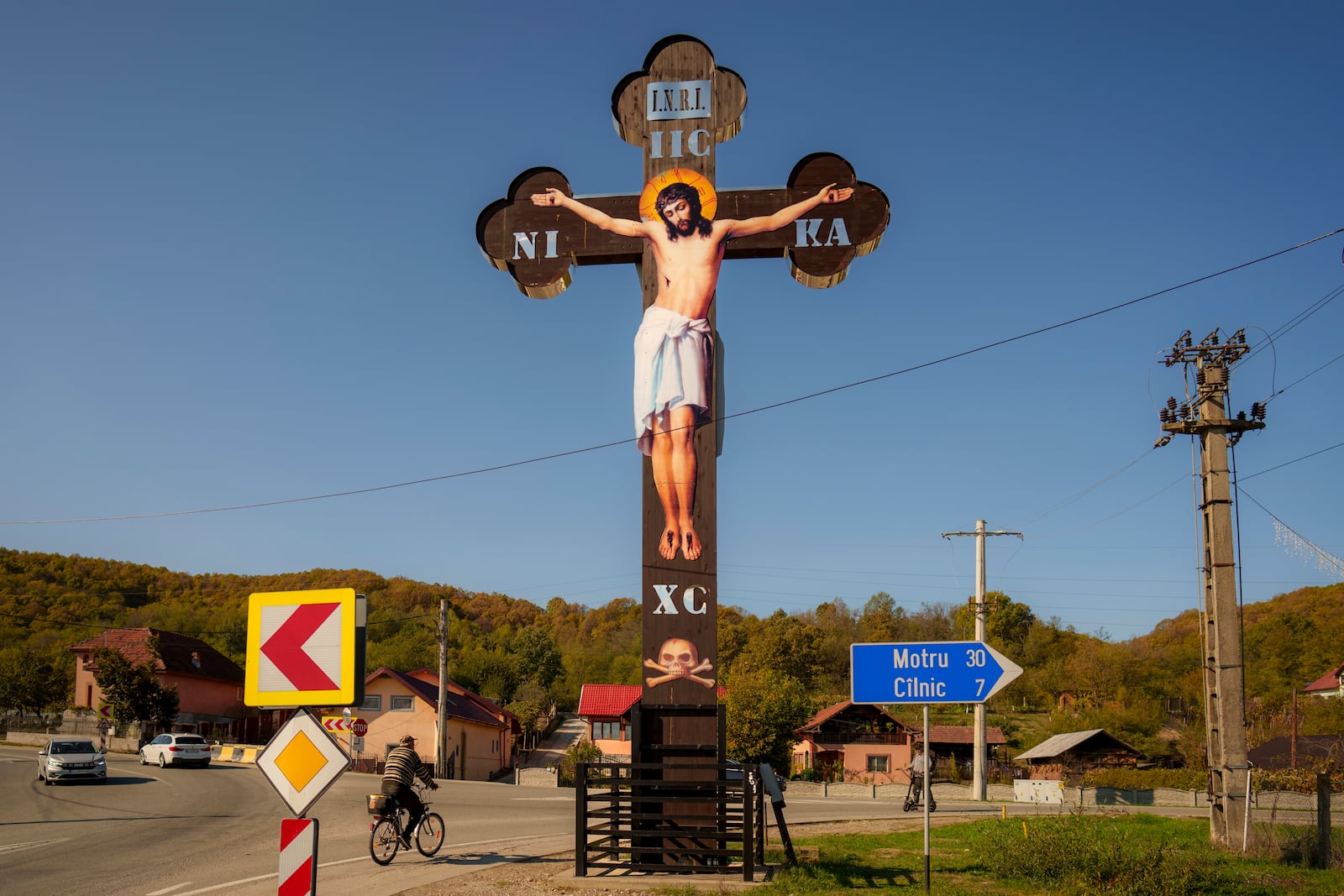 A man rides a bicycle past a large cross placed at an intersection in the village of Vart, southern Romania, Friday, Oct. 11, 2024. (AP Photo/Vadim Ghirda)