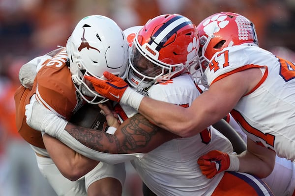 Texas quarterback Arch Manning, left, is tackled by Clemson defensive tackle Payton Page, center, and linebacker Sammy Brown, right, during the second half in the first round of the College Football Playoff, Saturday, Dec. 21, 2024, in Austin, Texas. (AP Photo/Eric Gay)