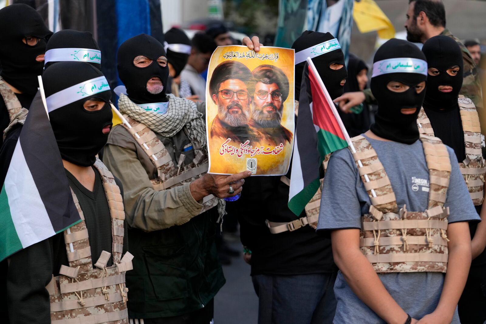 A group of the Iranian demonstrators cover their faces in the Palestinian and Lebanese militants style as one of them holds a poster of slain Hezbollah leader Hassan Narallah, right, and Hashem Safieddine, a powerful cleric who was expected to succeed Nasrallah and was killed by an Israeli airstrike in Beirut, in a ceremony commemorating the late Hamas leader Yahya Sinwar and Hashem Safieddine, at the Felestin (Palestine) Sq. in Tehran, Iran, Thursday, Oct. 24, 2024. (AP Photo/Vahid Salemi)