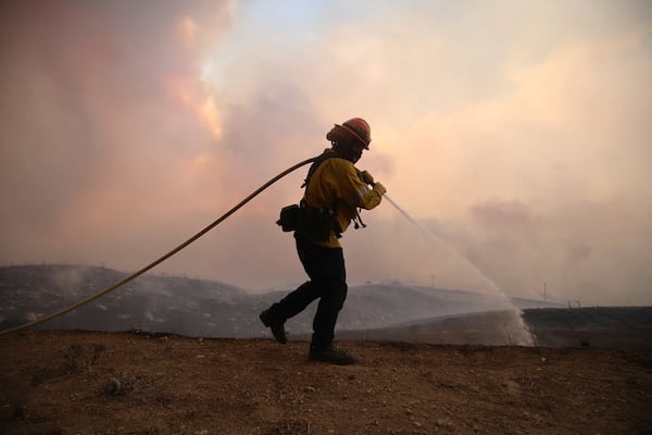 A firefighter sprays water on the ground while battling the Hughes Fire in Castaic, Calf., Wednesday, Jan. 22, 2025. (AP Photo/Ethan Swope)