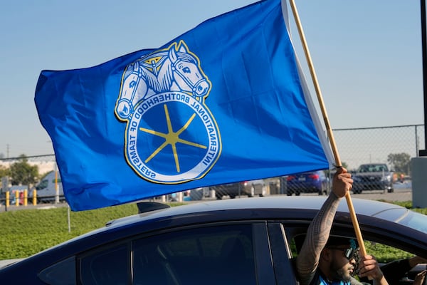 A supporter waving a Teamster flag rides past Amazon workers striking outside the gates of an Amazon Fulfillment Center on Friday, Dec. 20, 2024, in City of Industry, Calif. (AP Photo/Damian Dovarganes)