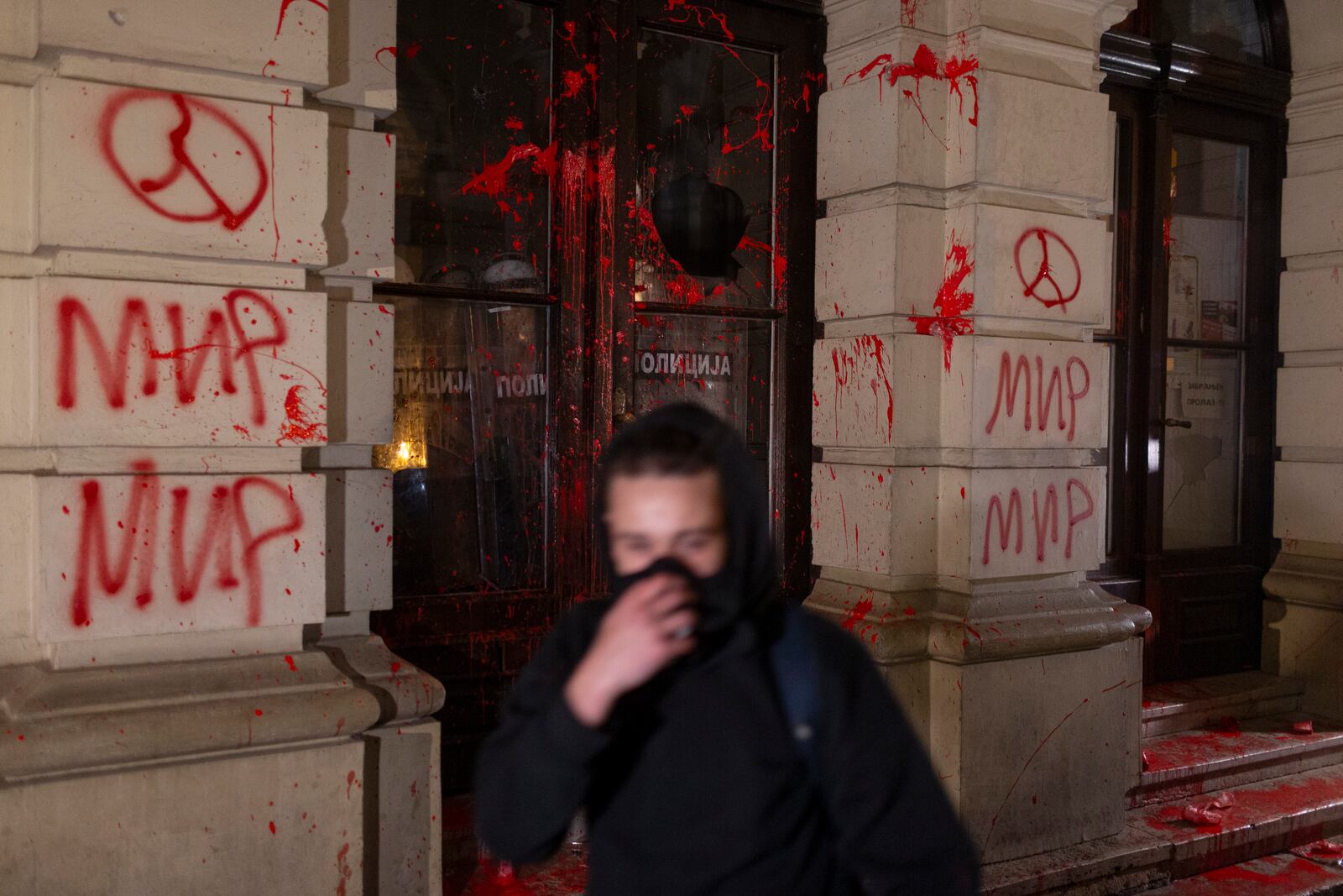 A protester passes by the City Hall building covered in red paint during a protest in Novi Sad, Serbia, Tuesday, Nov. 5, 2024. (AP Photo/Marko Drobnjakovic)