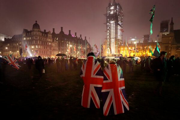 FILE - People draped in UK flags walks across Parliament Square during rainfall in London on Jan. 31, 2020. (AP Photo/Kirsty Wigglesworth, File)